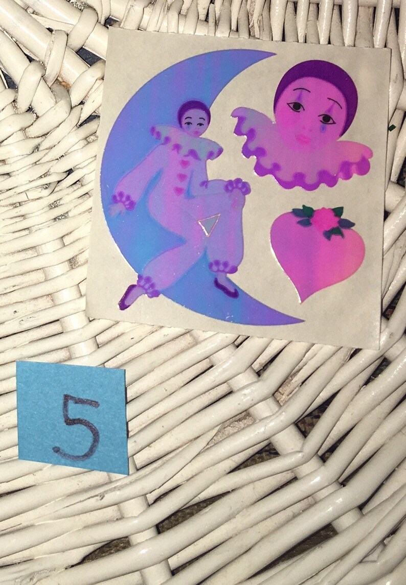 May include: A vintage sticker sheet with three holographic stickers. The stickers feature a purple and blue clown on a crescent moon, a purple and pink clown with a ruffled collar, and a pink heart with a pink flower.