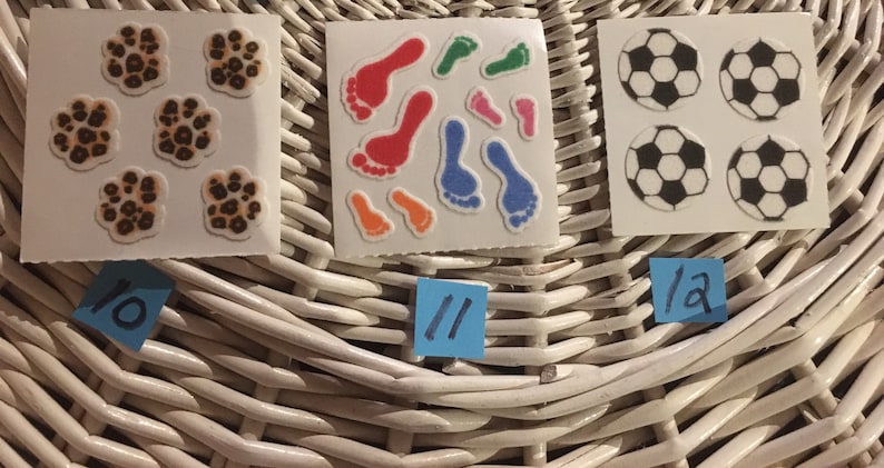 May include: Three sheets of stickers with different designs. The first sheet has five paw prints with a brown and orange leopard print. The second sheet has nine colorful footprints. The third sheet has four black and white soccer balls. The sheets are labeled with the numbers 10, 11, and 12.