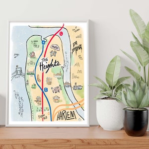 May include: A hand-drawn map of The Heights neighborhood in New York City, featuring landmarks and streets. The map is in a white frame and is hanging on a wall.