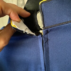 K&ouml;nnte beinhalten: Eine marineblaue Jacke mit einem schwarzen Rei&szlig;verschluss und einem gelben Besatz am Kragen.