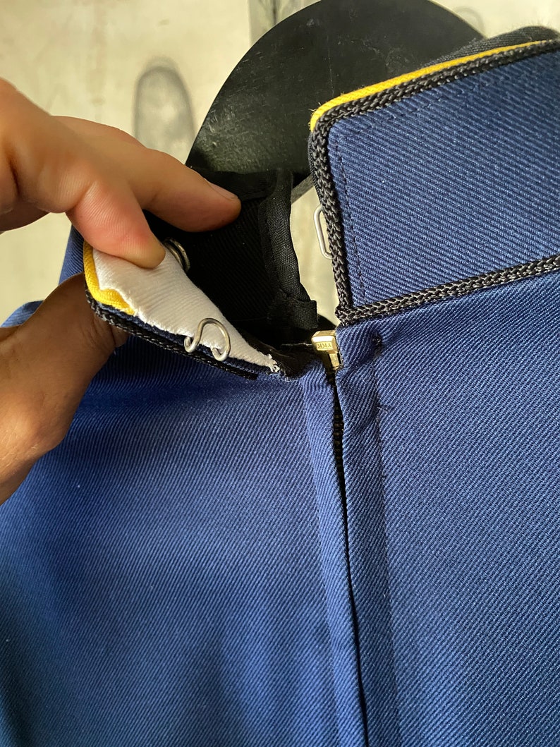 K&ouml;nnte beinhalten: Eine marineblaue Jacke mit einem schwarzen Rei&szlig;verschluss und einem gelben Besatz am Kragen.