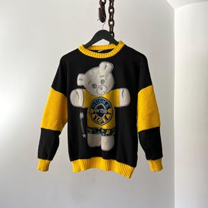 May include: Black and yellow knit sweater with a white teddy bear wearing a blue and yellow shirt with the text "Hug Me With Love".