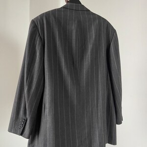 May include: A dark gray pinstripe blazer with a single button closure. The blazer is hanging on a wooden hanger with a chain.