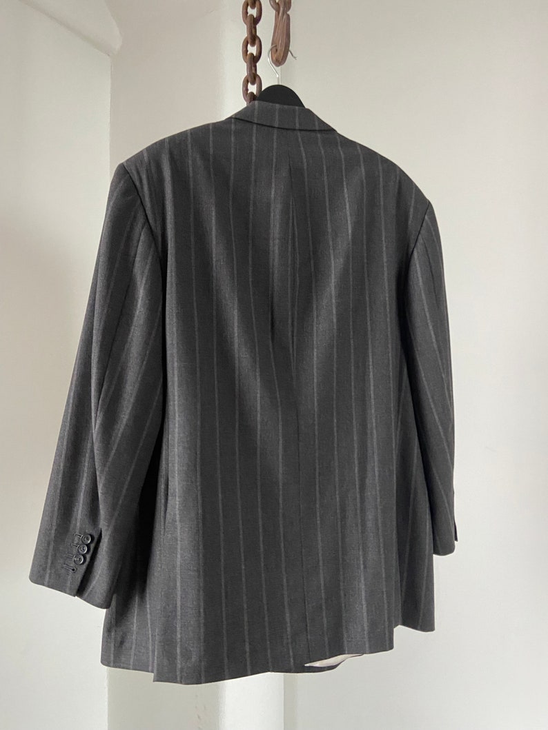 May include: A dark gray pinstripe blazer with a single button closure. The blazer is hanging on a wooden hanger with a chain.