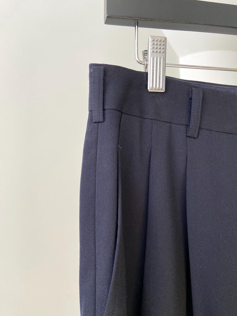 K&ouml;nnte beinhalten: Eine dunkelblaue, gefaltete Hose, die an einem Kleiderb&uuml;gel h&auml;ngt. Die Hose hat eine gerade Bein und einen klassischen Stil.
