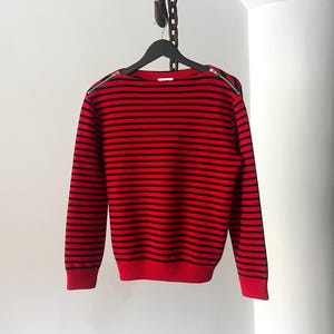 May include: Red and black striped sweater with zipper details on the shoulders.