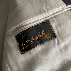 May include: A black label sewn into a white fabric lining with the text "Exclusively Tailored for A.V. Angell off" in white cursive lettering.