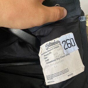 K&ouml;nnte beinhalten: Ein schwarzes Etikett mit wei&szlig;em Text, der "Stanbul Employee Owned Company", "260", "Brookfield, Missouri 64628", "Wearer No. 42R", "Size 260", "Order 24472-B", "Professional Dry Clean Only", "100% Polyester" und "11" lautet. Das Etikett enth&auml;lt auch den Text "Made in U.S.A." und "WPL9704".