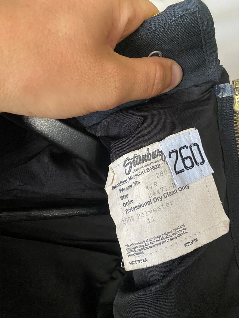 K&ouml;nnte beinhalten: Ein schwarzes Etikett mit wei&szlig;em Text, der "Stanbul Employee Owned Company", "260", "Brookfield, Missouri 64628", "Wearer No. 42R", "Size 260", "Order 24472-B", "Professional Dry Clean Only", "100% Polyester" und "11" lautet. Das Etikett enth&auml;lt auch den Text "Made in U.S.A." und "WPL9704".