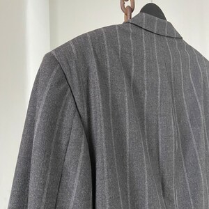 May include: A gray pinstripe blazer with a classic cut. The blazer is hanging on a hanger with a chain attached to the top.