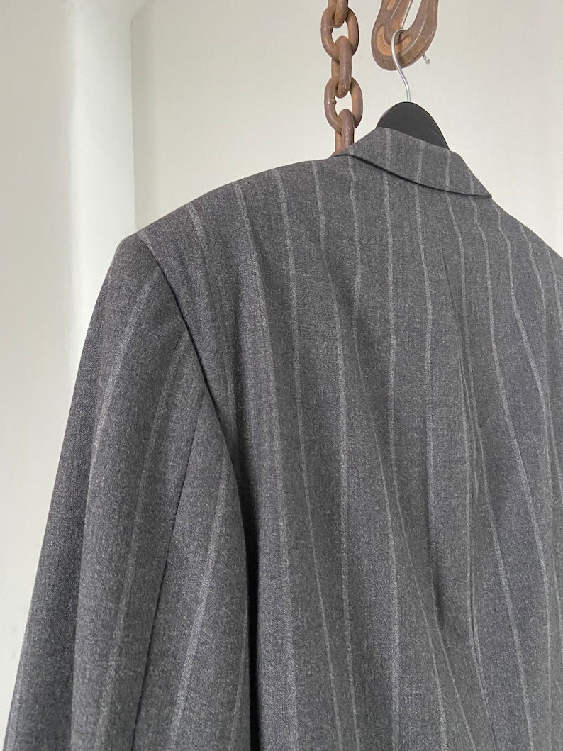 May include: A gray pinstripe blazer with a classic cut. The blazer is hanging on a hanger with a chain attached to the top.