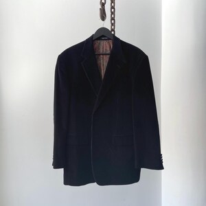 May include: A black velvet blazer hanging on a black hanger. The blazer has a classic two-button design with notched lapels and two front pockets. The interior lining features a patterned design.