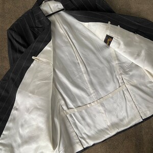 May include: A black and white striped blazer with a white satin lining. The blazer has a double breasted closure and a pocket on the inside.
