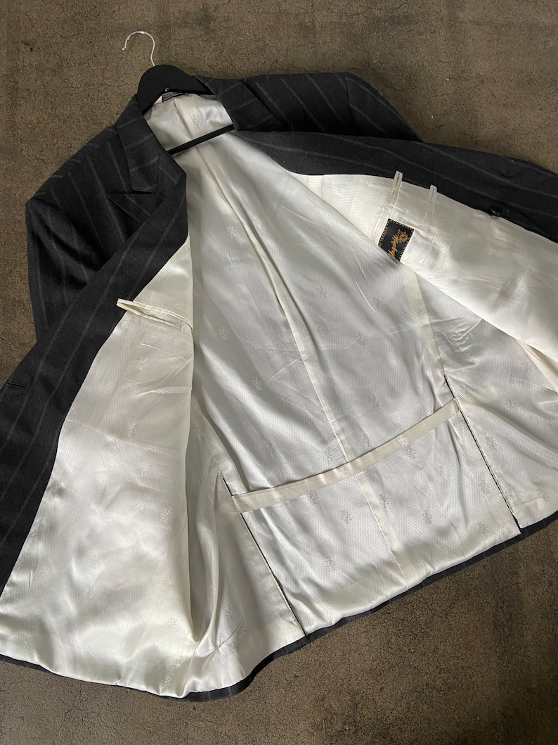 May include: A black and white striped blazer with a white satin lining. The blazer has a double breasted closure and a pocket on the inside.
