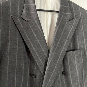 May include: A double-breasted gray blazer with thin white pinstripes. The blazer has a notch lapel and two button closures.