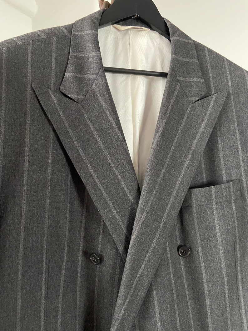 May include: A double-breasted gray blazer with thin white pinstripes. The blazer has a notch lapel and two button closures.