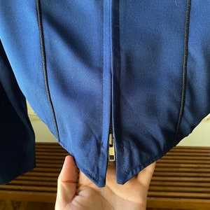 K&ouml;nnte beinhalten: Eine marineblaue Jacke mit Rei&szlig;verschluss und schwarzen N&auml;hten entlang der N&auml;hte.