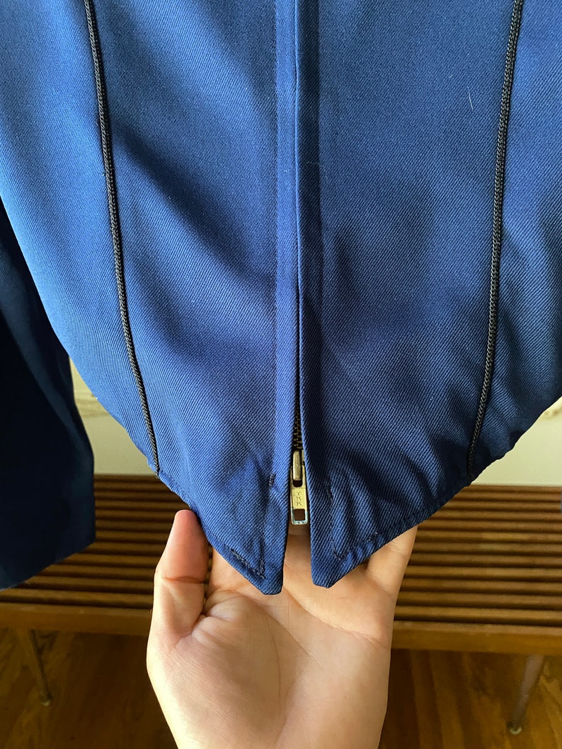 K&ouml;nnte beinhalten: Eine marineblaue Jacke mit Rei&szlig;verschluss und schwarzen N&auml;hten entlang der N&auml;hte.