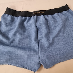 May include: Blue boxer shorts with a black elastic waistband. The waistband has the text "Underwear For Men" printed on it.