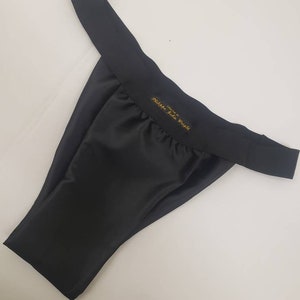 Peut inclure: Sous-vêtements en satin noir avec une étiquette dorée indiquant "Victoria's Secret"