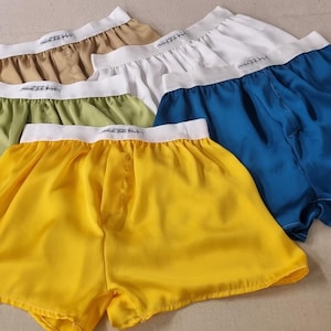 以下が含まれることがあります： 黄色、緑、ベージュ、白、青のサテンボクサーパンツのコレクション。各ペアは、テキストがプリントされた白いウエストバンドが特徴です。ショーツは光沢のある滑らかな生地で作られています。