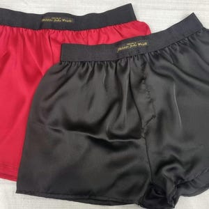 Puede incluir: Dos pares de calzoncillos de satén, uno rojo y otro negro. Los calzoncillos tienen una cintura elástica con una etiqueta dorada que dice "Made for People".