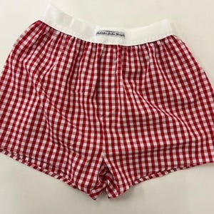 May include: Red and white gingham boxer shorts with a white waistband. The shorts have a classic check pattern and a comfortable, relaxed fit. The waistband features a small label with text.