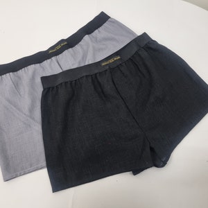May include: Two pairs of boxer shorts, one grey and one black. Both have a gold elastic waistband with the text "Milano di Paris" printed on them.