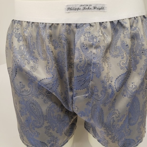 Peut inclure: Boxer en soie gris avec un motif paisley bleu. La ceinture est blanche avec le texte "Création de Philippe John Wright" en noir.