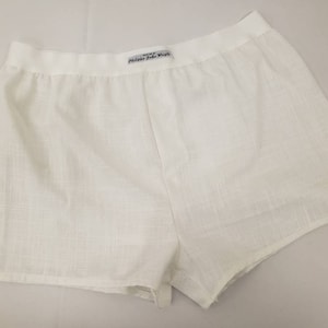 May include: White cotton shorts with a wide elastic waistband. The waistband has a small white tag with the text "Made in Italy, Philippe Jude Paris".