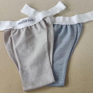 Op de afbeelding: Twee paar ondergoed met witte elastische taillebanden. Een paar is lichtgrijs en het andere is lichtblauw. Het lichtgrijze paar heeft een label met de tekst "Made with Love by Wright".