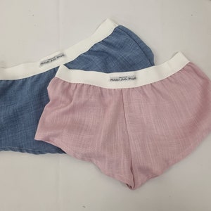 Puede incluir: Dos pares de ropa interior, uno azul y otro rosa, con cinturas elásticas blancas. La cintura tiene el texto "Creado por Philippa John Wright" impreso.