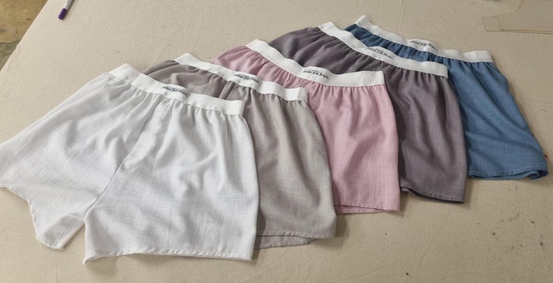 May include: Six pairs of boxer shorts in a variety of colours, including white, grey, pink, and blue. The shorts are made from a soft, lightweight fabric and have a comfortable elastic waistband.