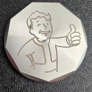 May include: A silver-colored metal coin with a laser-engraved image of a cartoon character giving a thumbs up. The character has short, spiky hair and is wearing a collared shirt.