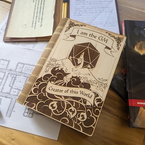 May include: A wooden journal with an engraved design of a phoenix and a twenty-sided die. The journal has the text "I am the GM Creator of this World" on the front cover.