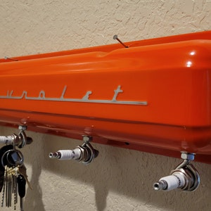 May include: Orange Chevrolet valve cover key holder with four spark plug hooks.