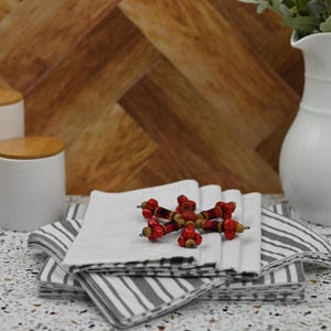 May include: A stack of white and black striped kitchen towels with a red and brown beaded snowflake decoration on top.