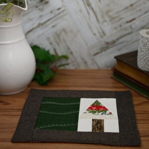 Peut inclure: Un dessous de plat rectangulaire fait à la main avec une bordure marron foncé. Le centre présente une section verte avec des coutures blanches et une section blanche avec un motif d'arbre. L'arbre a un sommet à motifs rouge et blanc et un tronc en bois.