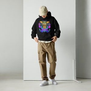 May include: Black hoodie with a colorful graphic design on the front. The graphic features a central face-like image with vibrant blues, purples, yellows, and greens. The person is wearing khaki cargo pants and a beige baseball cap.
