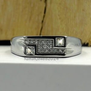 May include: A silver band ring with a geometric design featuring a row of small clear stones and two larger square clear stones.