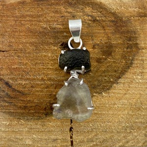 Puede incluir: Un colgante de plata con una piedra verde oscura y una piedra verde claro. Las piedras están engastadas en plata y el colgante tiene una anilla de plata.