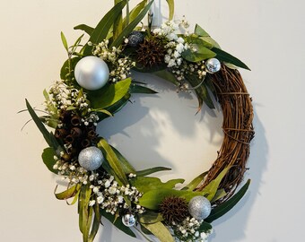 May include: A silver and green Christmas wreath with silver ornaments and white flowers.