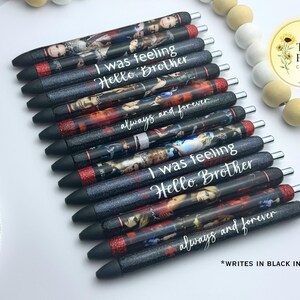 Pu&ograve; includere: Un set di 12 penne nere con accenti di glitter rosso. Ogni penna presenta un'immagine e un testo diversi, tra cui "I was feeling Hello, Brother" e "always and forever". Le penne scrivono con inchiostro nero.