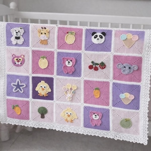 May include: A handmade baby blanket with a patchwork design. Each square features a different embroidered animal or food item, including a bear, giraffe, panda, and ice cream cone. The blanket is in shades of pink, purple, and white, with a white crocheted border.