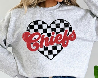 May include: A light gray sweatshirt featuring a heart-shaped design with a black and white checkered pattern. The word "Chiefs" is printed in red, stylized lettering across the heart. The sweatshirt is a crew neck style.