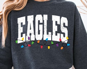 May include: Dark gray sweatshirt with the word "EAGLES" in white block letters. Below the word is a string of colorful Christmas lights. The sweatshirt is a crew neck style.