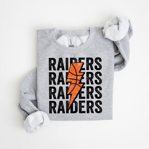 May include: Gray sweatshirt with a black and orange basketball lightning bolt graphic and the text "RAIDERS" repeated four times.