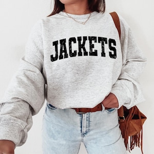 May include: A gray sweatshirt with the word "JACKETS" printed in black on the front. The sweatshirt has a relaxed fit and long sleeves.