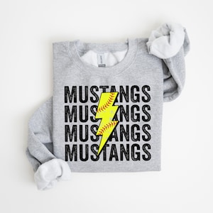 May include: Gray sweatshirt with a black and yellow lightning bolt graphic. The lightning bolt is made up of a softball. The text "MUSTANGS" is repeated four times in black.