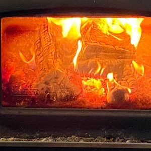 Pu&ograve; includere: Una vista ravvicinata di una stufa a legna con un fuoco incandescente all'interno. Le fiamme sono arancioni e gialle, e le  ceppi ardono vivacemente.